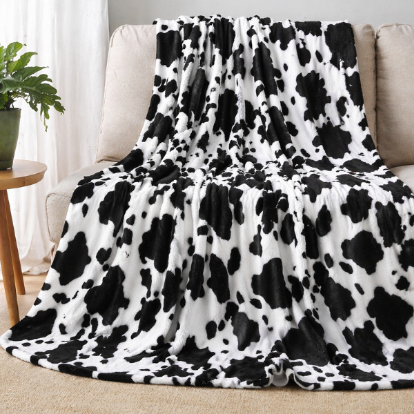 Weiße, flauschige Kuscheldecke mit schwarzen Kuhflecken liegt über einem Sofa ausgebreitet.